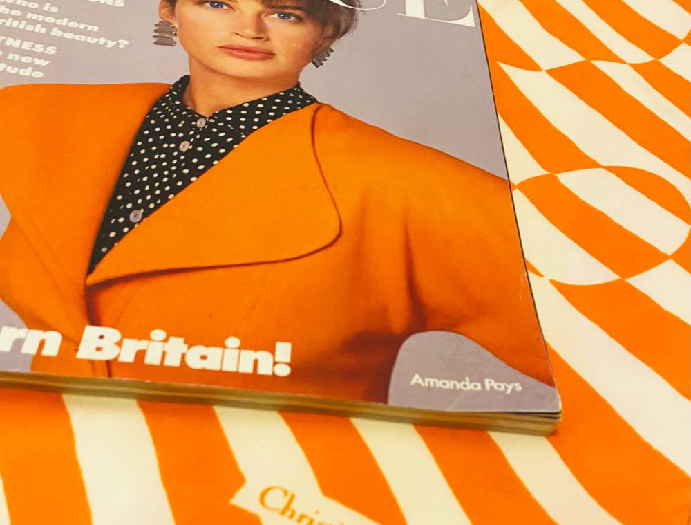 Vintage Vogue magazine with a cover featuring a woman in an orange coat on an orange and white striped background.